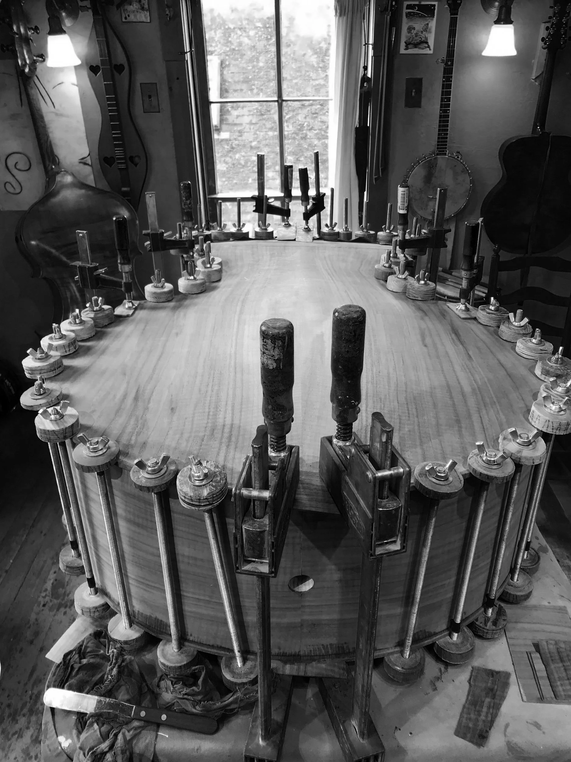 A woodworking project in progress, showing a large wooden round table being glued and clamped with several clamps around its circumference.